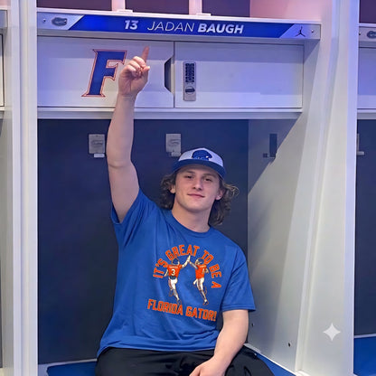 A young man sitting in a locker wearing a blue Florida Gators t-shirt and a blue cap, pointing upward. The locker has '13 JADAN BAUGH' on the top shelf.