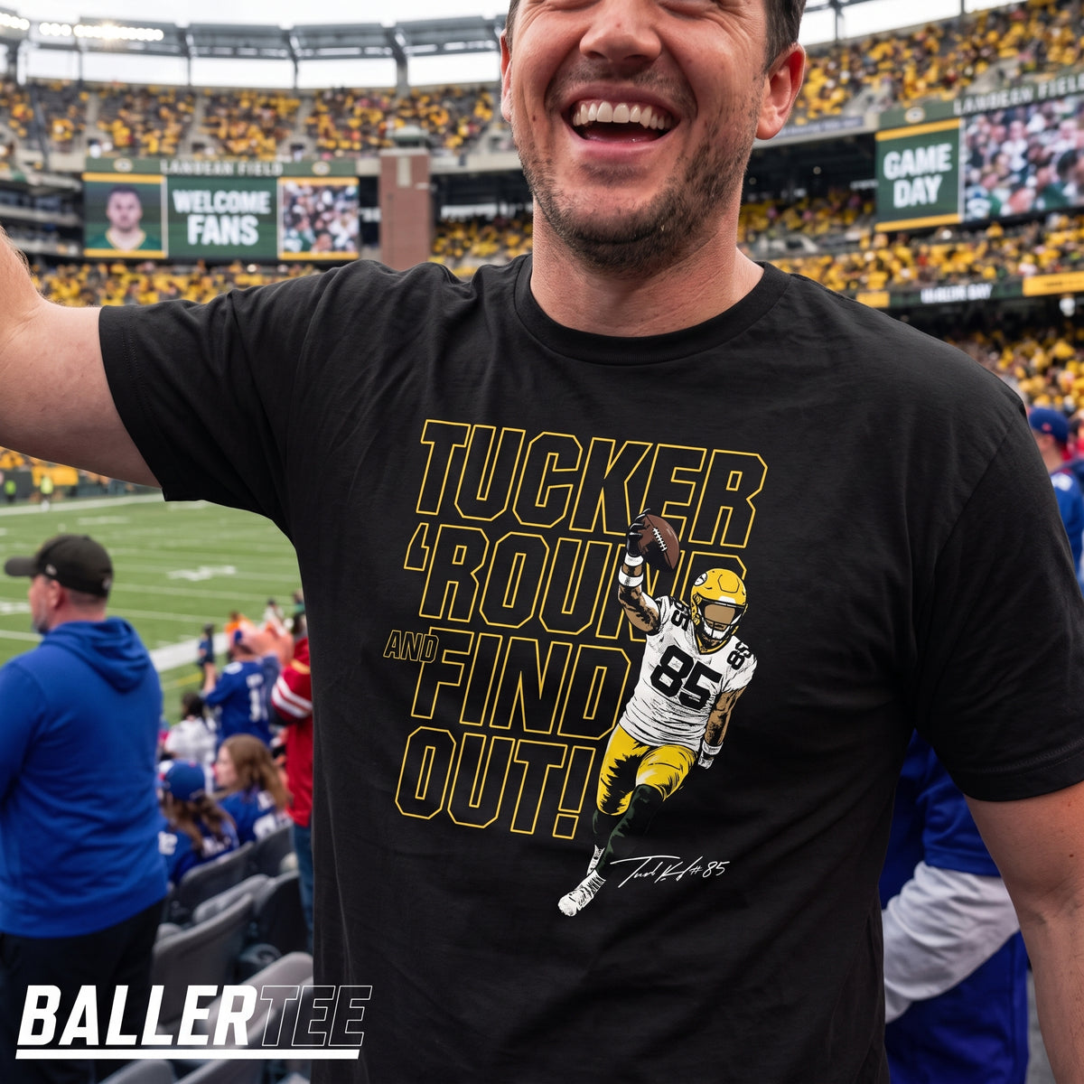 A man wearing a black graphic t-shirt at a football stadium. The shirt features a graphic of quarterback Tucker Kraft in a green and gold Oakland Raiders uniform with the text 'TUCKER 'ROUND AND FIND OUT!' in yellow and white.