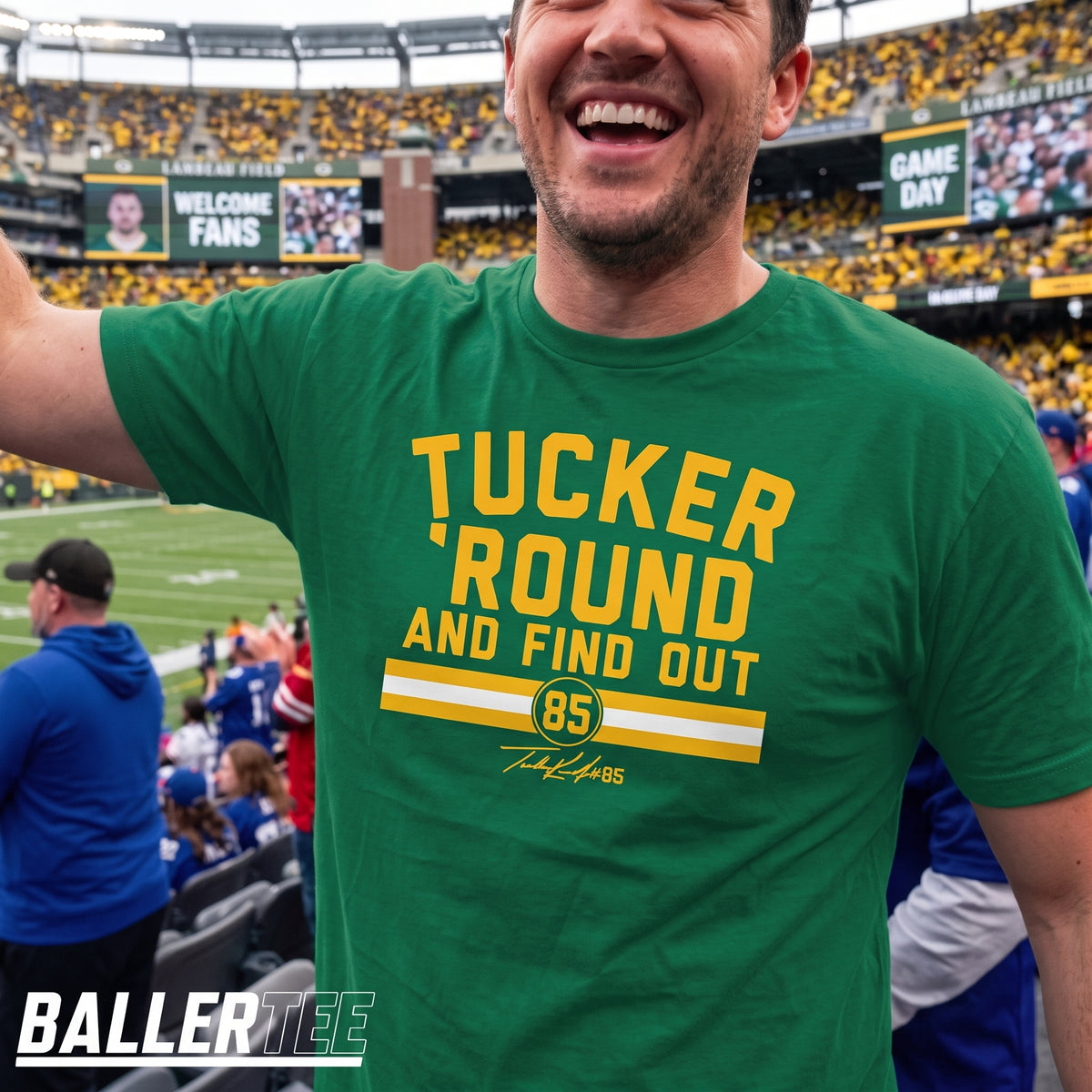 A man wearing a green Baller Tee t-shirt with yellow text reading 'TUCKER ROUND AND FIND OUT 85' at a football stadium. The background shows a crowded stadium with fans and signs.