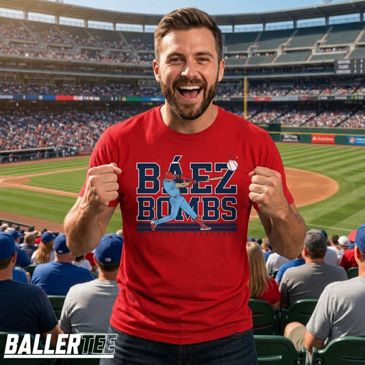 A man in a red baseball stadium wearing a red graphic t-shirt that says 'BÉEZ BOMBS' with a blue baseball player graphic. The background shows a packed baseball stadium.