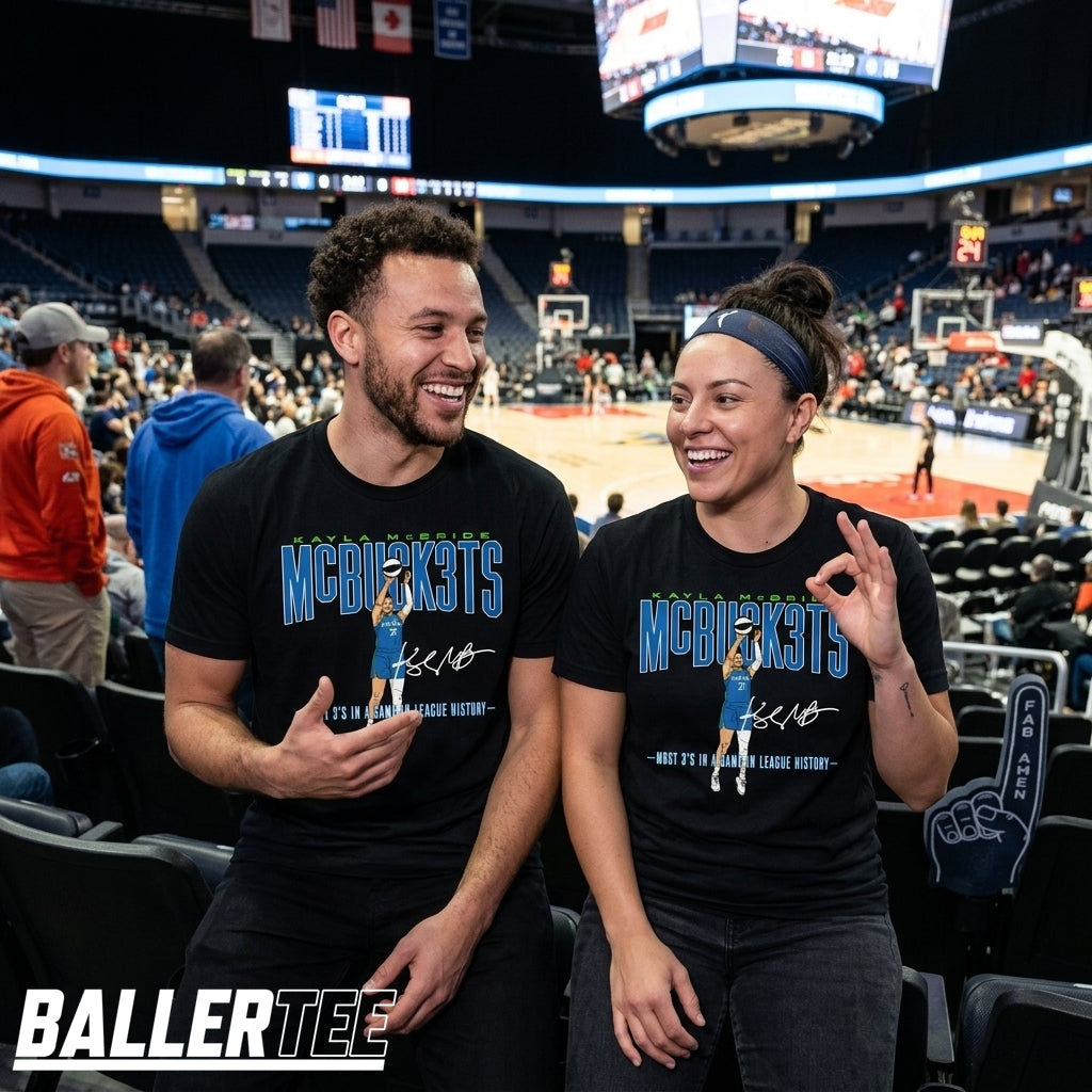 Two people sitting in an arena wearing matching black graphic T-shirts with a blue and green 'MCKICKS' design and a small player illustration. The background shows a basketball court and stadium seating.