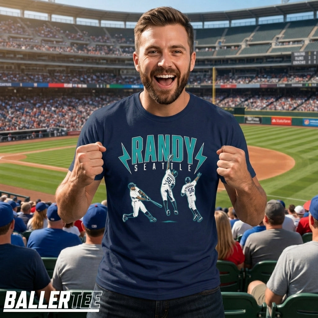 A man wearing a navy blue graphic t-shirt with a baseball player design and the text 'RANDY SEATTLE' stands in a crowded baseball stadium. The BallerTee logo is visible in the bottom-left corner.