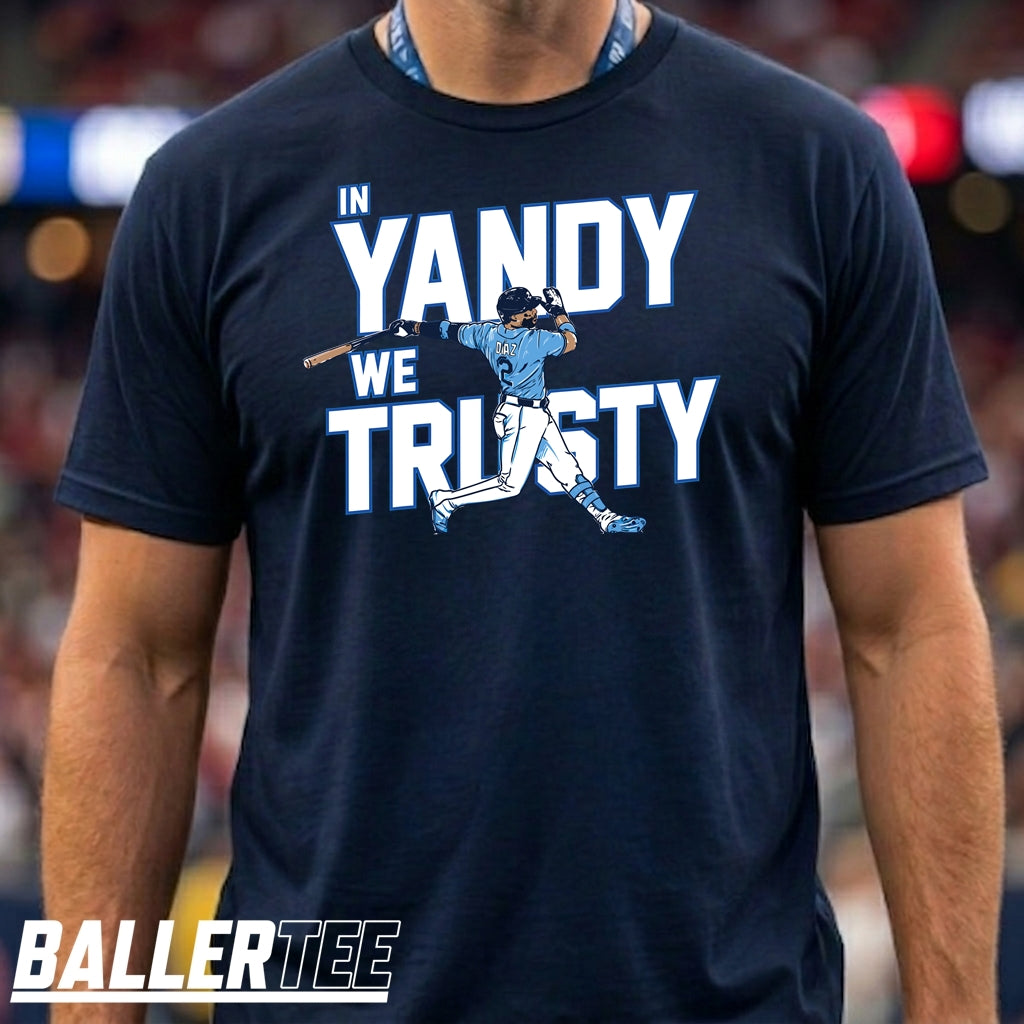 A man wearing a navy blue t-shirt with a graphic that reads 'IN YANDY WE TRUSTY' in white and light blue, featuring a baseball player illustration. The brand 'BALLERTEE' is visible as an overlay at the bottom left.