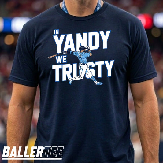 A man wearing a navy blue t-shirt with a graphic that reads 'IN YANDY WE TRUSTY' in white and light blue, featuring a baseball player illustration. The brand 'BALLERTEE' is visible as an overlay at the bottom left.